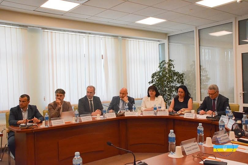 Учасники зустрічі за круглим столом: сім осіб сидять за столом із табличками й пляшками води.